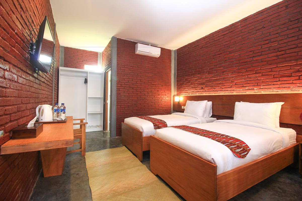 Una habitación de hotel con una pared de ladrillo, un escritorio de madera, dos camas y un espejo.