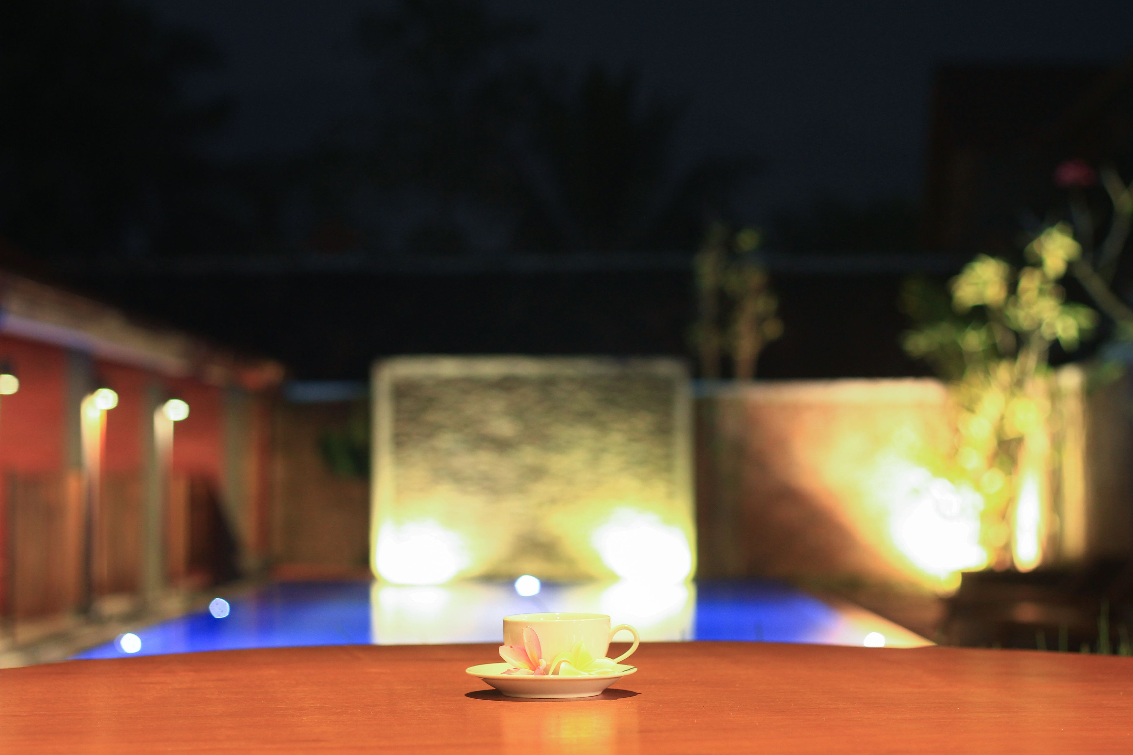 Une tasse posée sur une table, avec un arrière-plan flou composé de lumières et d’un bâtiment.