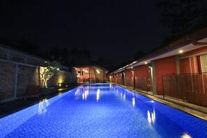 Relax by the illuminated pool surrounded by a brick wall and a wooden fence.