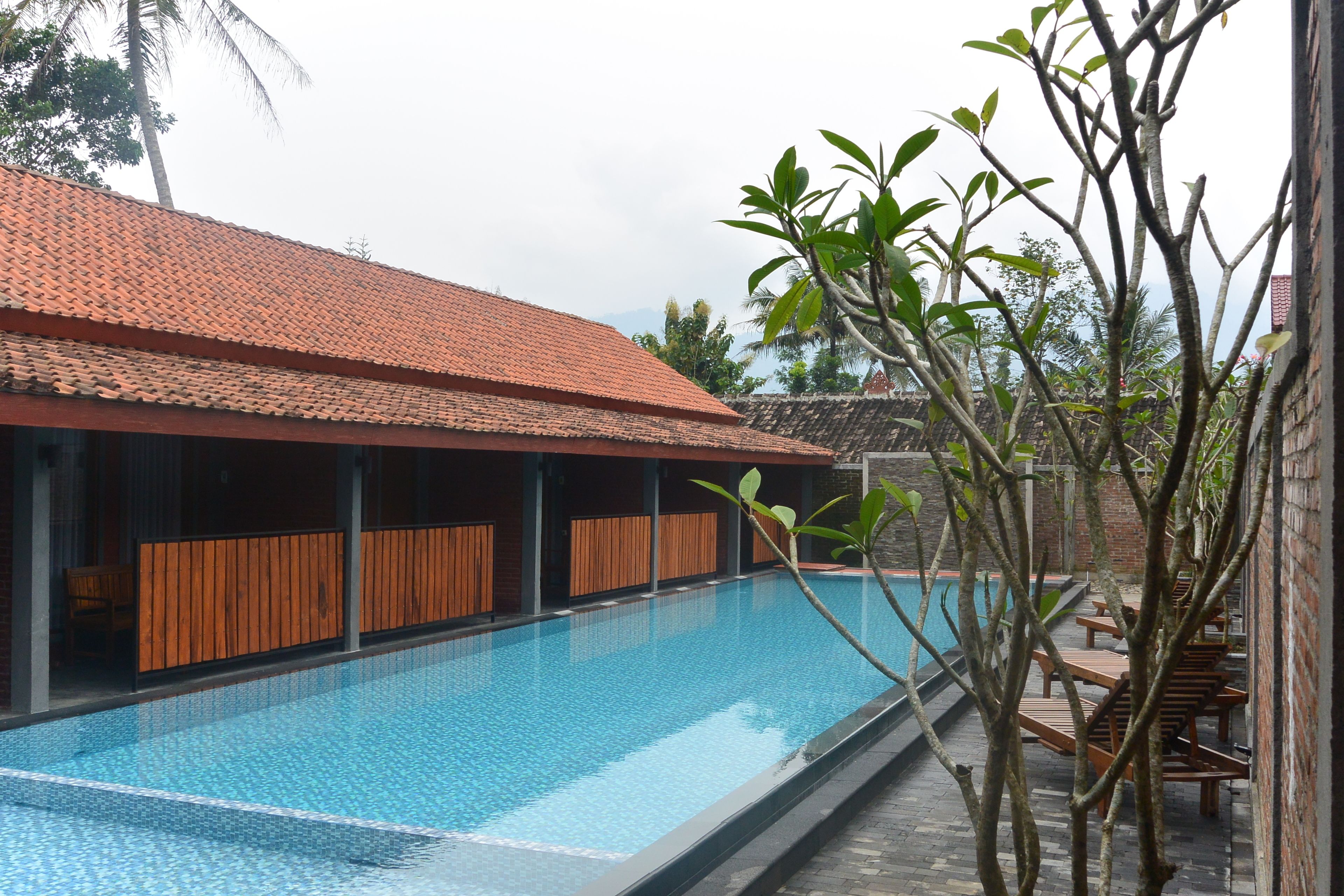 A swimming pool with a tiled roof, wooden deck seating, and a brick wall.