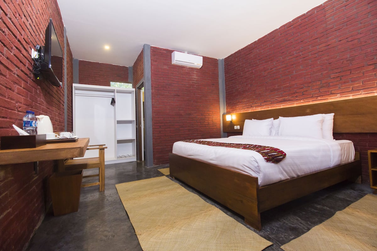 Una habitación de hotel con pared de ladrillo, cama de madera, escritorio con silla y armario.