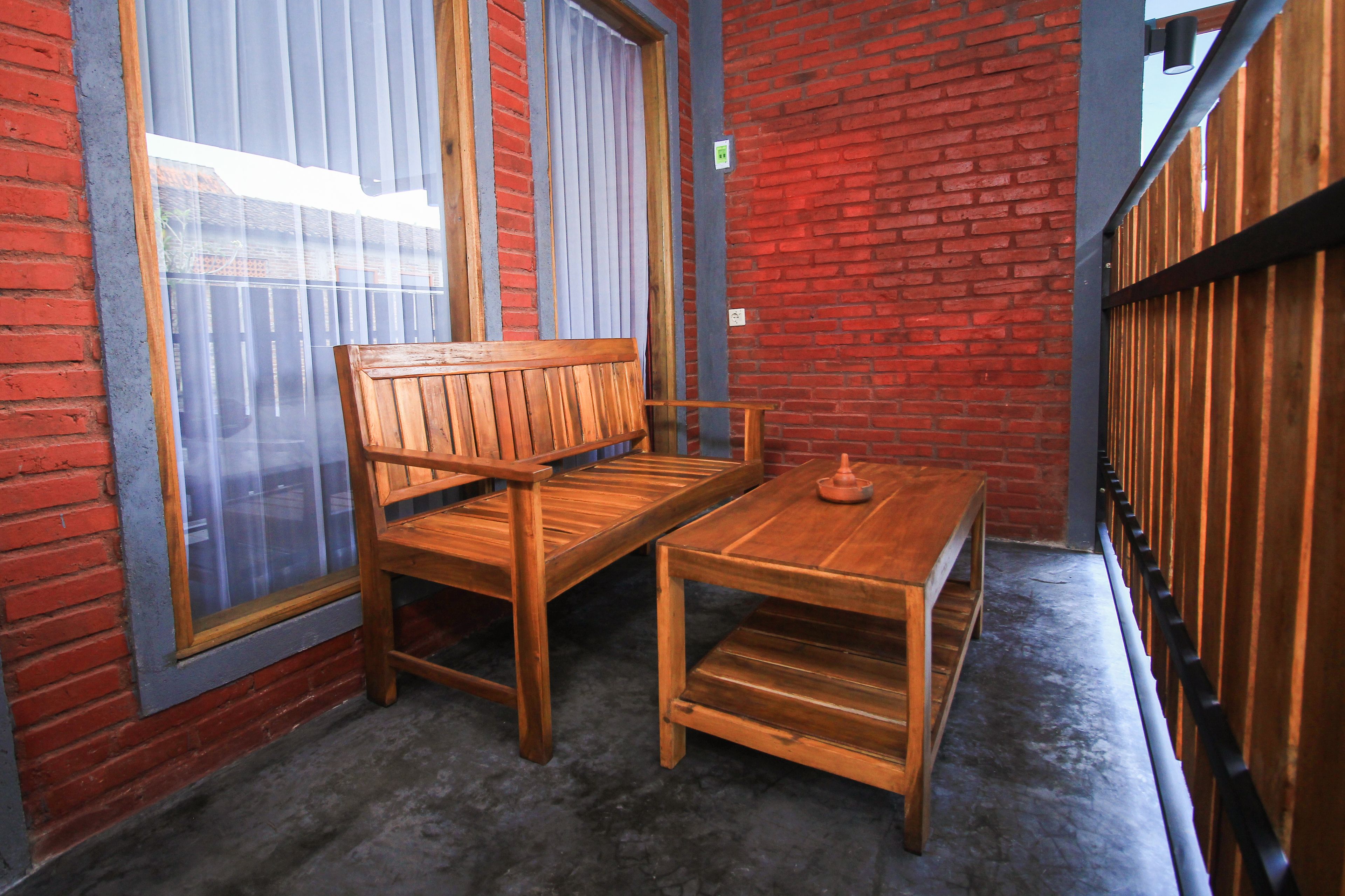 Un banco y una mesa de madera frente a un muro de ladrillo rojo con una ventana y persianas.