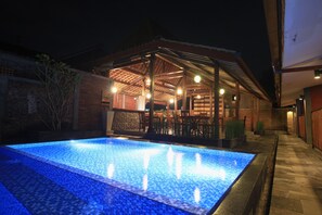A swimming pool with a tiled edge, a covered patio area with chairs, and a brick wall. - Wahid Borobudur (Borobudur)