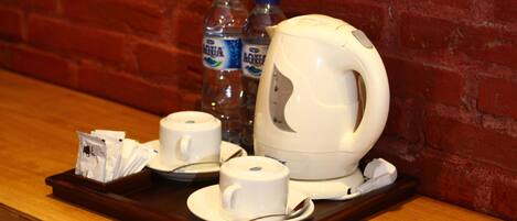 A breakfast tray with two white cups, a teapot, and two bottles of water on a wooden table against a brick wall.