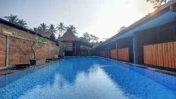 Una piscina con superficie de agua cristalina y azul, rodeada de muros de ladrillo y vallas de madera.