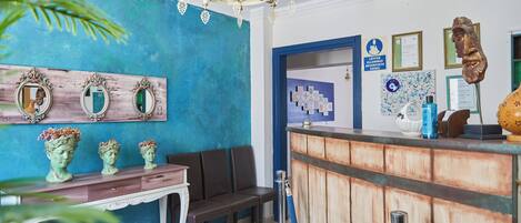 Un área de recepción con mostrador de madera, una araña de cristal y una pared azul con espejos decorativos.
