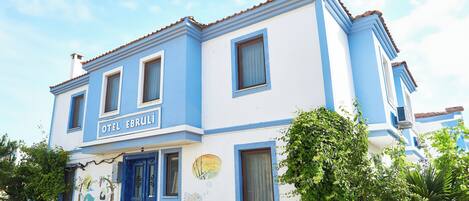 Un edificio de dos pisos con fachada azul y blanca, una puerta azul y un cartel que dice 'OTEL EBRULI'.
