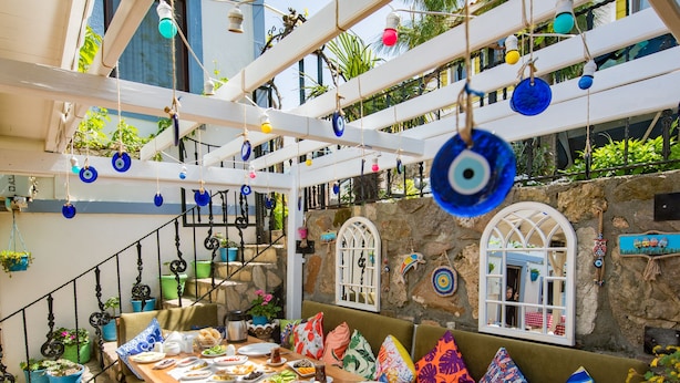 A wooden table set with plates and a bench with colorful cushions. - Ebruli Hotel (Bozcaada)
