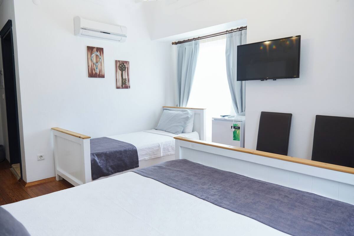 A hotel room with a bed, a TV, and a window with curtains.