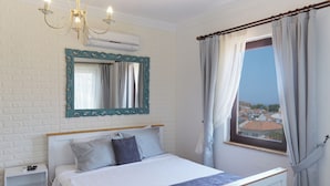 A bedroom with a bed, a nightstand, a mirror, and a window with curtains. - Ebruli Hotel (Bozcaada)