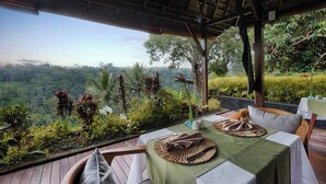 Un área de comedor al aire libre con una mesa dispuesta para dos personas, con vistas a un paisaje exuberante.