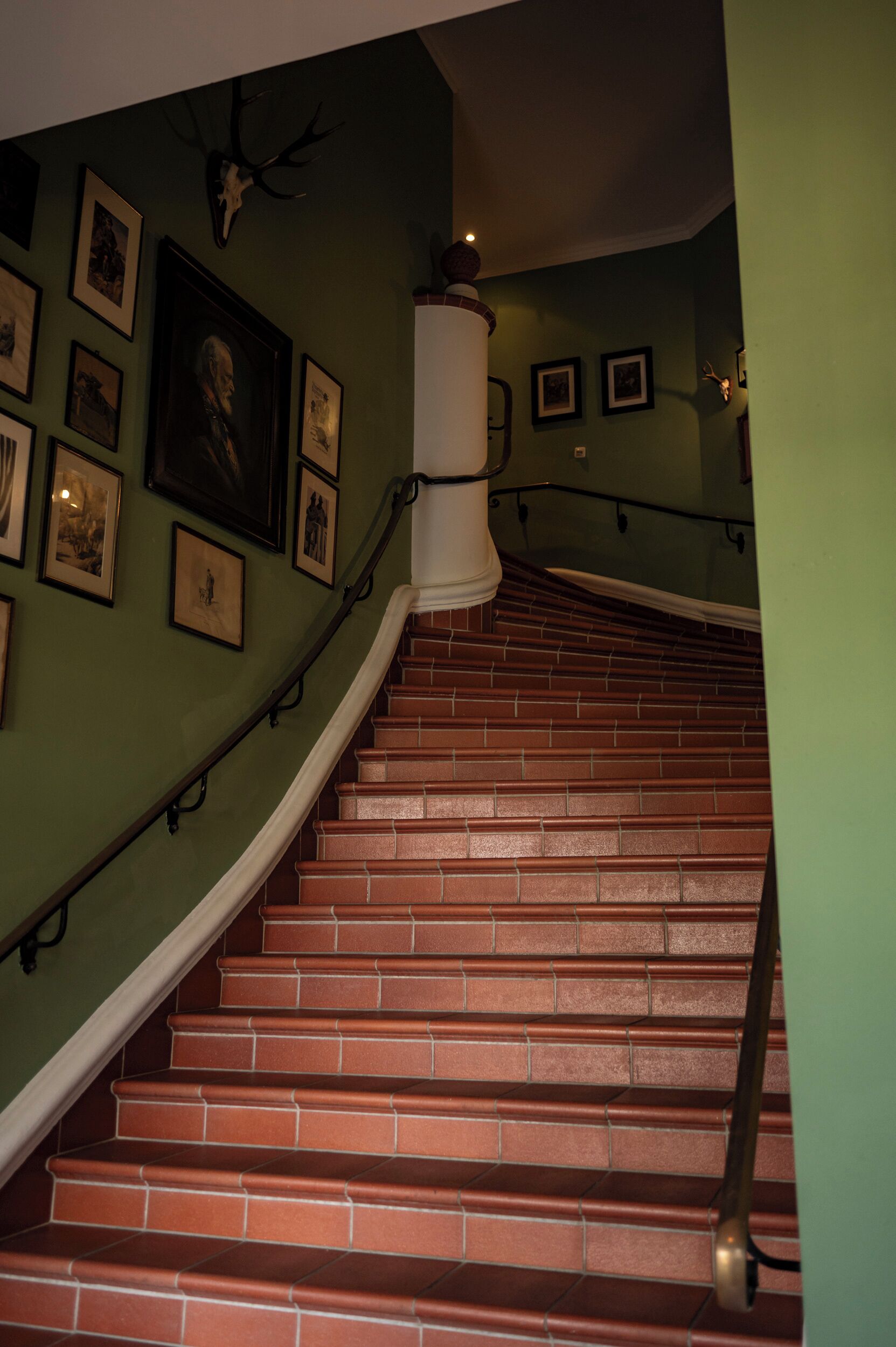 Eine Treppe mit roten Backsteinstufen, einem weißen Geländer und grünen Wänden, die mit gerahmten Bildern geschmückt sind.