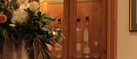 A wooden cabinet with glass doors, a metal vase with flowers, and a framed picture on the wall.