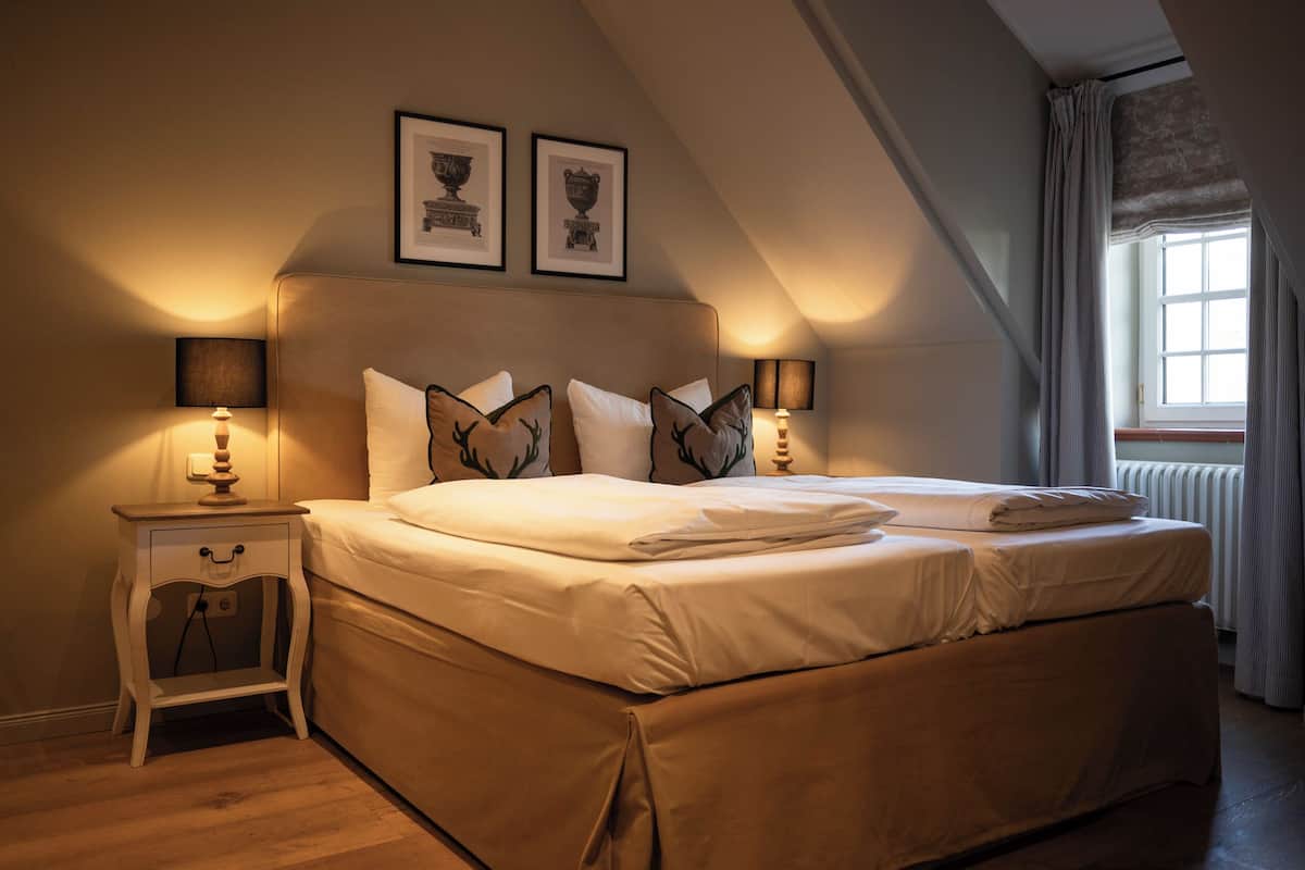 A bedroom with two beds, a nightstand, and a window with curtains.