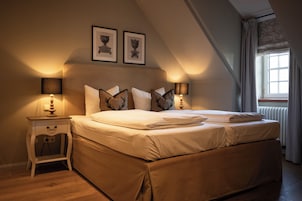 Quarto com duas camas, uma mesa de cabeceira e janela com cortinas.
