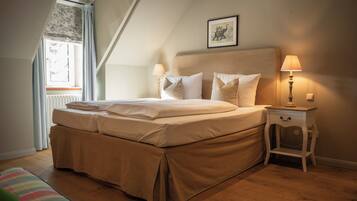 A bedroom with a large bed, two bedside tables with lamps, a window with curtains, and a framed picture on the wall.