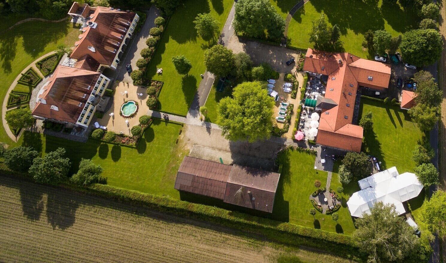 An aerial view of a property with multiple buildings, a swimming pool, and well-maintained gardens.