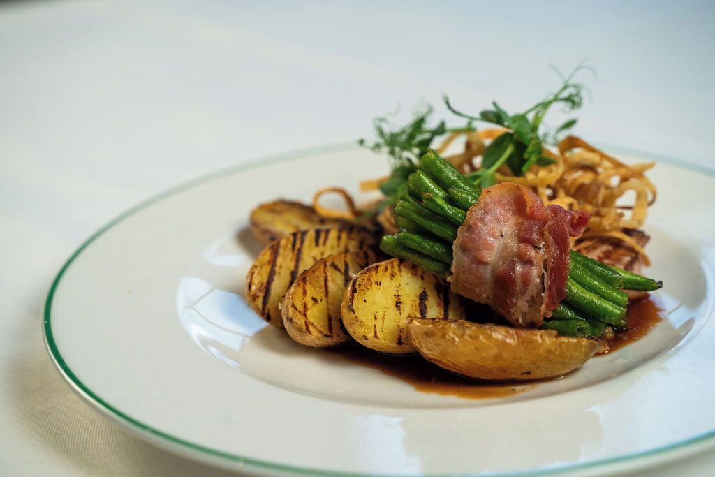 A plate with grilled potatoes, green beans, and a piece of bacon.