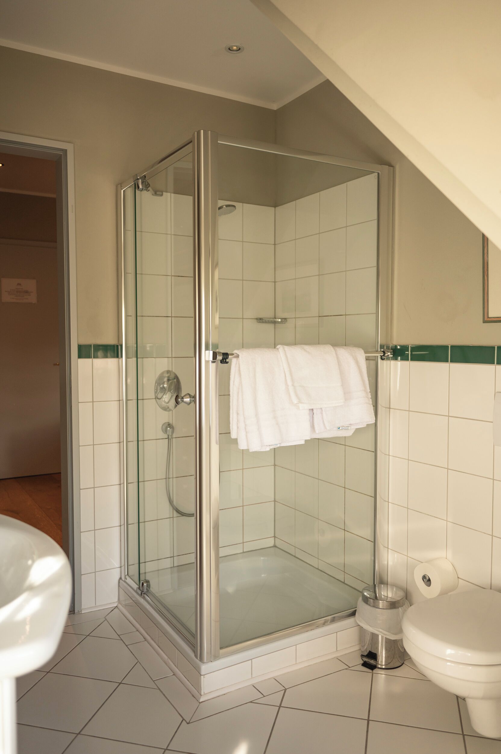 Un baño moderno con cabina de ducha de vidrio, azulejos blancos, un inodoro y un lavamanos.