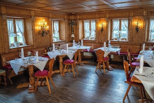 Restaurante com paredes revestidas de madeira, várias mesas dispostas com toalhas brancas, velas e cadeiras com almofadas vermelhas.