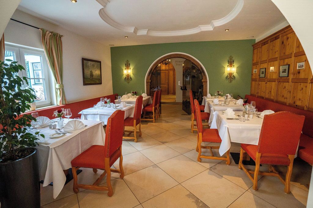 Un comedor con mesas dispuestas para cuatro, sillas tapizadas rojas y una pared verde con un panel de madera a la derecha.