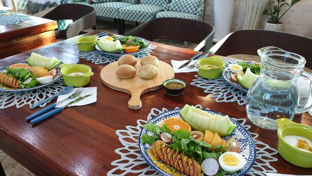 A dining table set with various dishes, including salads, fruits, and bread rolls. - Wind Jeju Cafe & Pension (Seogwipo)
