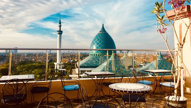 Varanda com área de estar externa, vista para a paisagem urbana incluindo uma cúpula e um minarete em destaque, e céu claro.