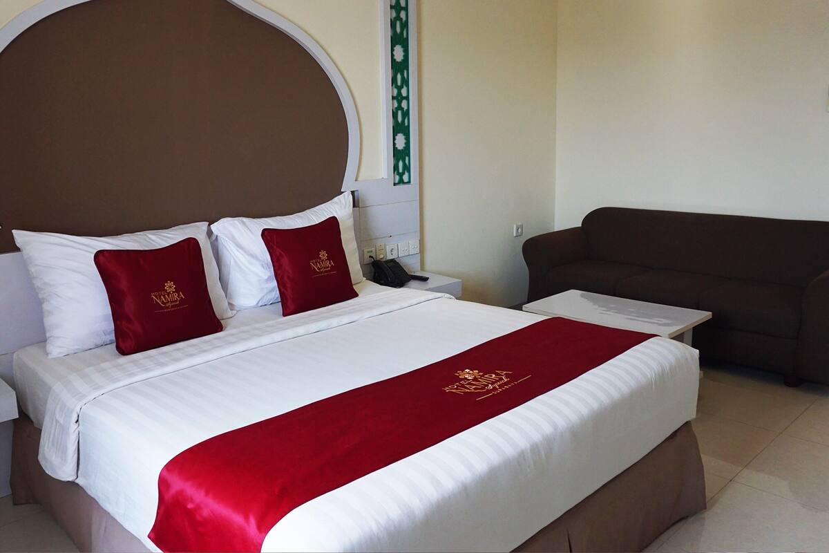 Una habitación de hotel con una cama grande, un cabecero marrón y una colcha roja y blanca.