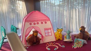 Een speelruimte met een tent, een glijbaan en diverse speelgoed, waaronder knuffels en voertuigen.