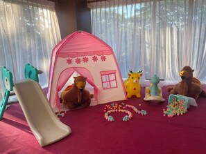 Un área de juegos con una carpa, un tobogán y varios juguetes, incluyendo peluches y vehículos.