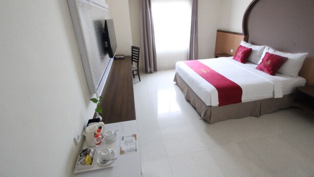 Hotelkamer met een groot bed, een flatscreen televisie, een bureau met stoel en een raam met gordijnen.