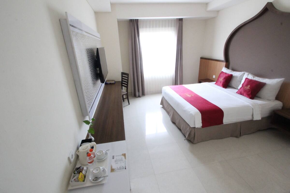 Habitación de hotel con una cama grande, televisión de pantalla plana, escritorio con silla y ventana con cortinas.