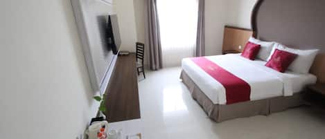 Quarto de hotel com uma cama grande, televisão de tela plana, escrivaninha com cadeira e janela com cortinas.