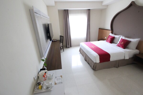 Habitación de hotel con una cama grande, televisión de pantalla plana, escritorio con silla y ventana con cortinas.