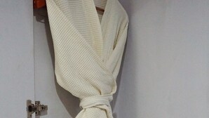 Een witte badjas hangt aan een houten kapstok voor een witte deur.