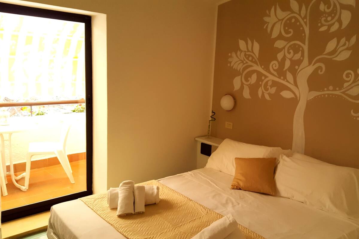 Een hotelkamer met een bed, nachtkastje, muurschildering en balkon met een stoel.