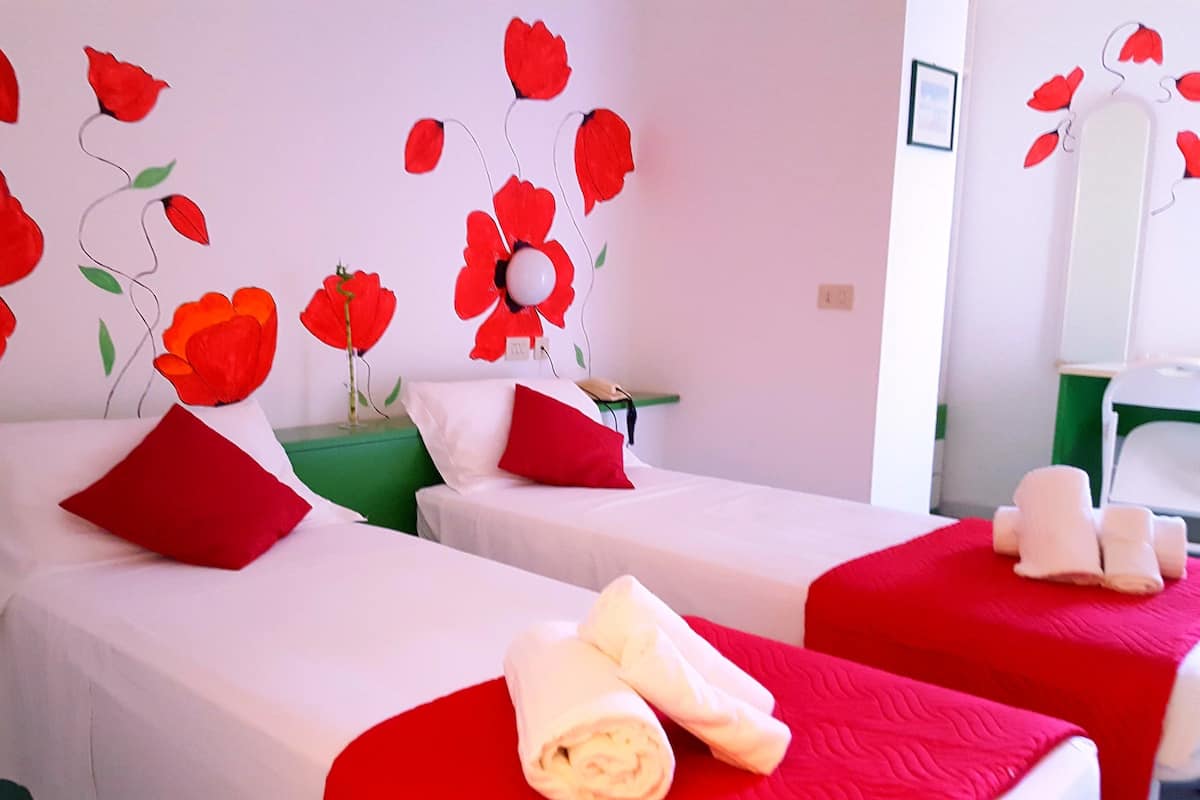 Een hotelkamer met twee bedden, rood-wit beddengoed en bloemen behang in rood.