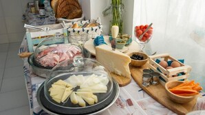 A breakfast buffet with various cheeses, meats, and fruits.