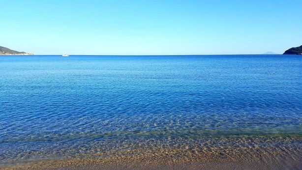 A clear view of a beach with calm water, a distant boat, and a clear sky.