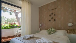 A hotel room with a bed, a nightstand, a window with a view of a balcony, and a wall-mounted decoration.