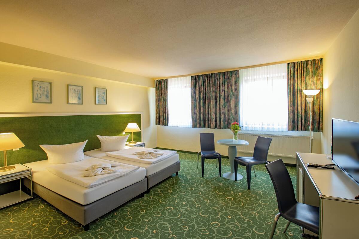Een hotelkamer met twee bedden, een bureau, een stoel, een tafel en een raam met gordijnen.