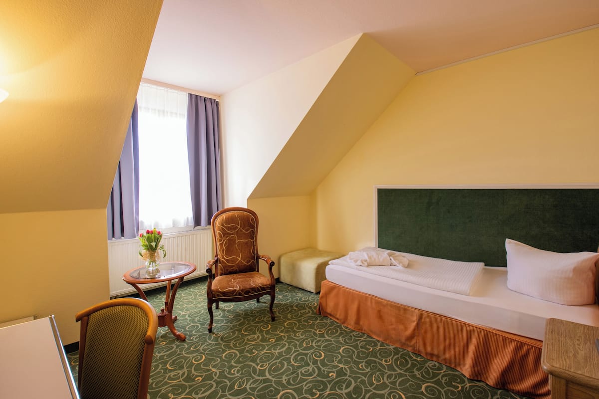 Een hotelkamer met een bed, een stoel, een klein tafeltje met een bloemenvaas en een radiator.