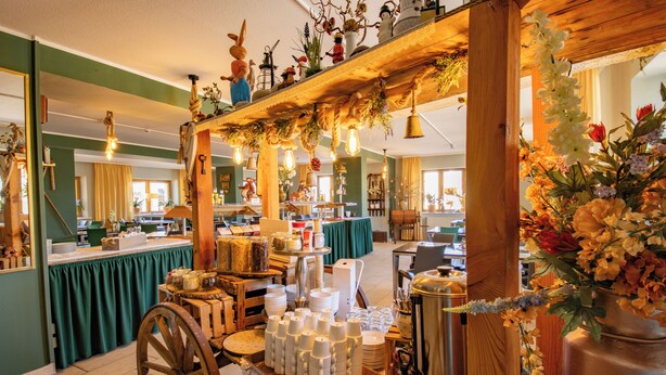 Un restaurante con una barra de madera rústica, una variedad de platos y bebidas, y una zona de comedor verde al fondo.