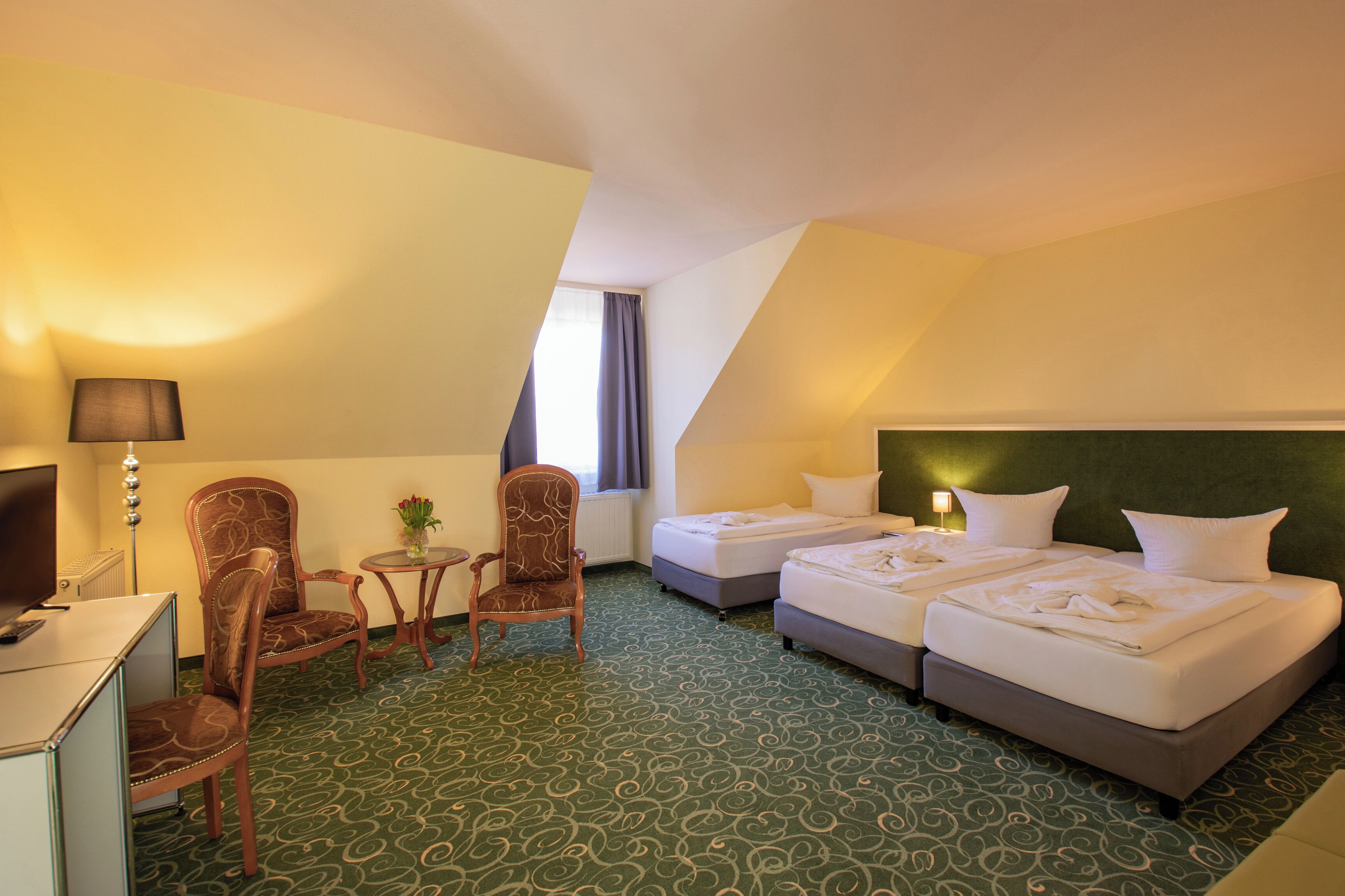 Hotellihuone, jossa on kaksi sänkyä, työpöytä, tuoli ja lamppu.