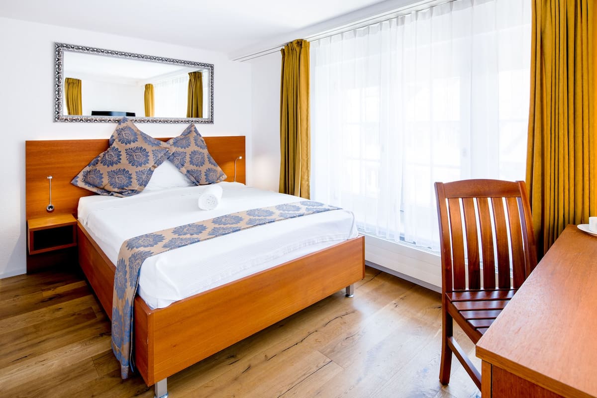 A hotel room with a wooden bed, a nightstand, a wooden chair, and a table.