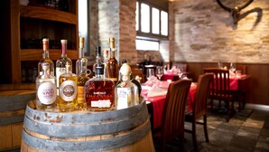 A bar area with bottles of alcohol on a barrel, wooden shelves, and a rustic brick wall with a mounted animal head. - Hotel Old Town (Zürich)
