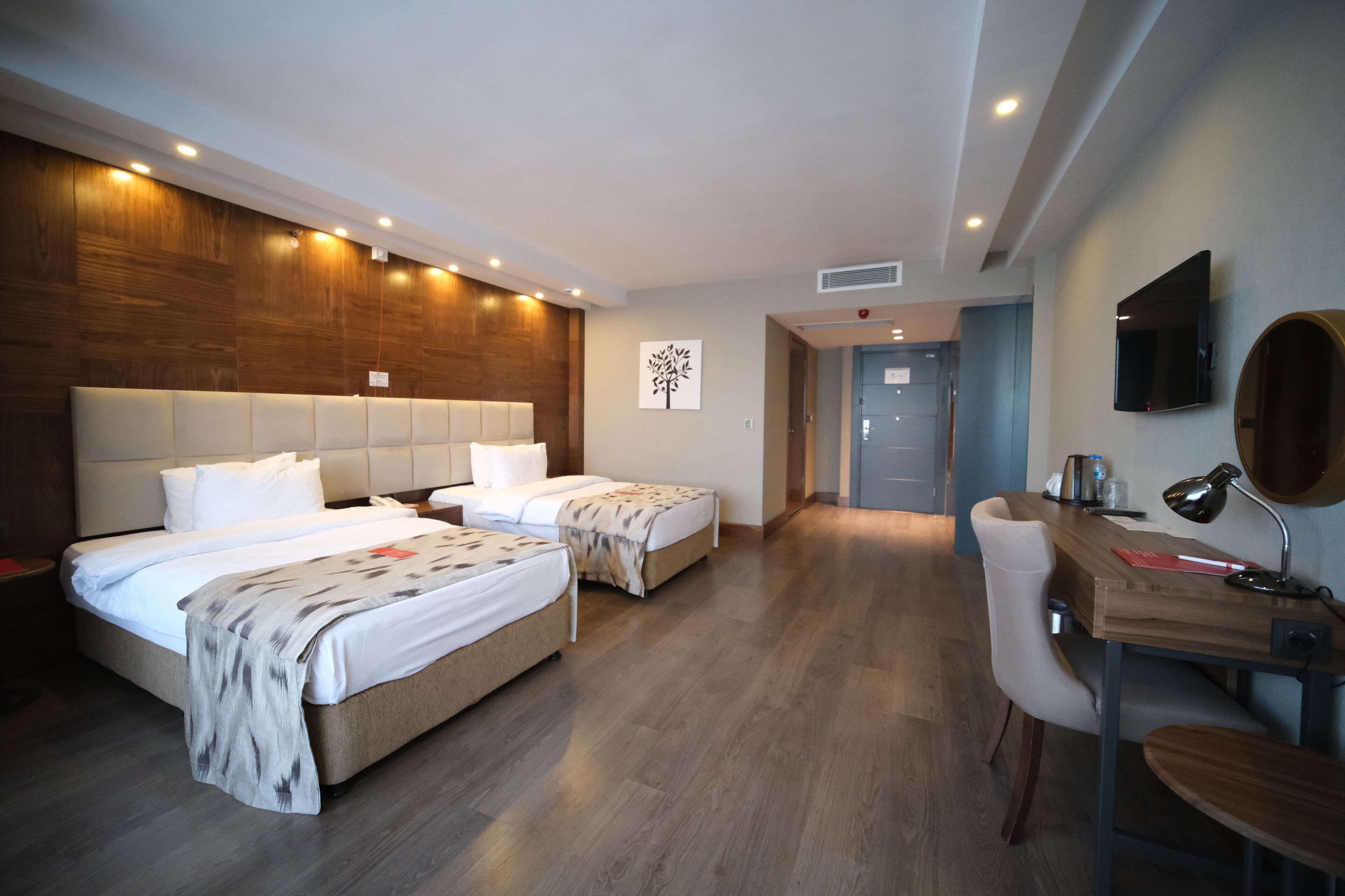 A hotel room with two beds, a desk, a chair, a TV, and a wooden accent wall.