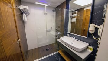 A modern bathroom with a glass-enclosed shower, a white sink, and a hairdryer mounted on the wall.