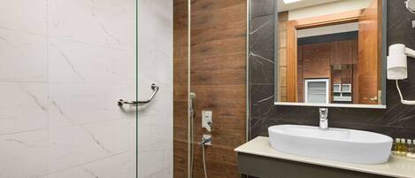 Un baño moderno con ducha envuelta en vidrio, lavamanos blanco y tocador de madera.