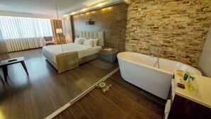 Una habitación de hotel moderna con una cama grande, una zona de estar separada, una bañera y una pared de piedra.